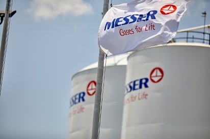Messer flag waving in front of gas storage tanks with Messer logo and slogan “Gases for Life” visible under a blue sky